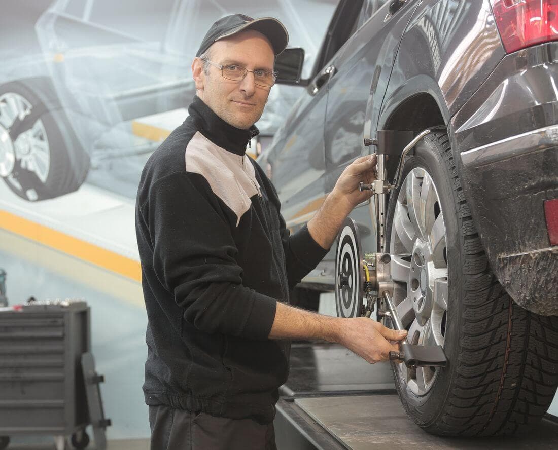 Meccanico che regola l'assetto di una ruota dell'auto con il calibro in officina