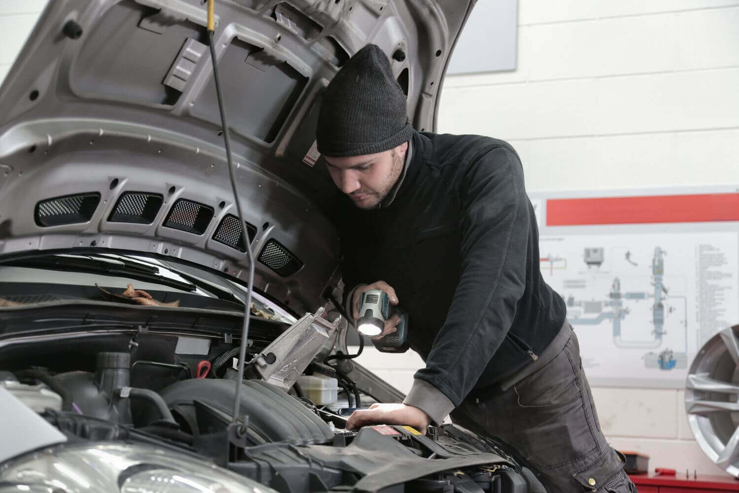 Meccanico dell'officina con lampada da lavoro mentre controlla il vano motore di un'auto sul ponte