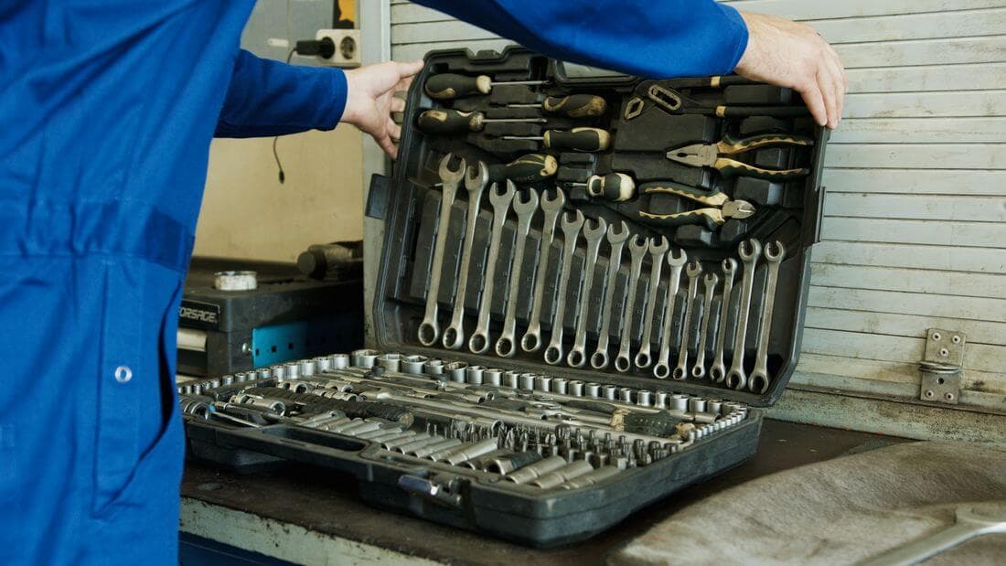 Meccanico in tuta che apre la cassetta degli attrezzi con chiavi e bussole in officina
