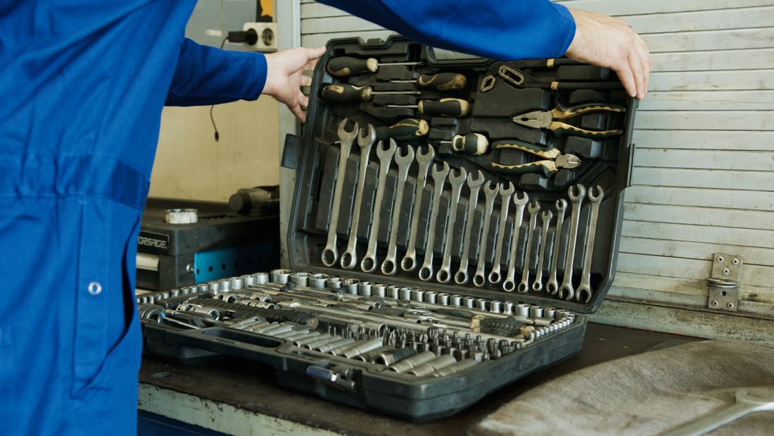 Meccanico in tuta che apre la cassetta degli attrezzi con chiavi e bussole in officina
